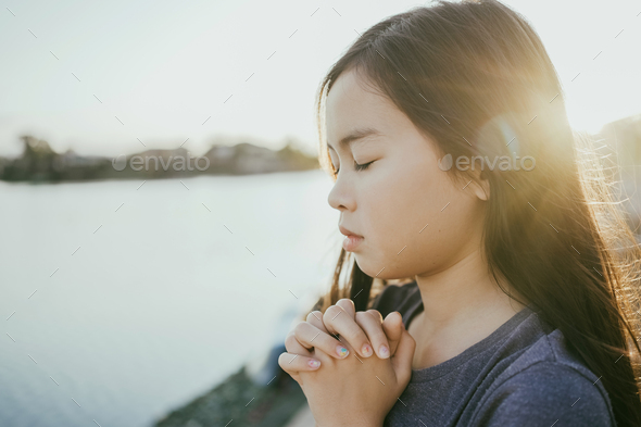 Preteen mixed girl praying with eyes closed by lake,peace and hope concept
