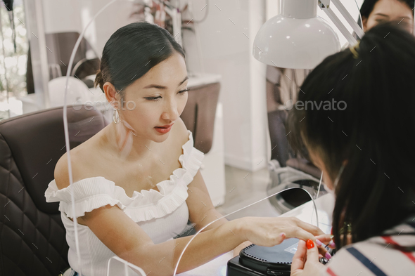 Asian woman client getting a manicure in nail salon,with protective screen,beauty lifestyle concept