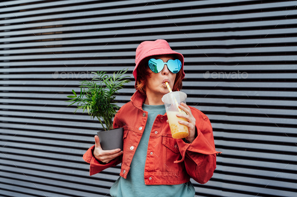 Hipster fashion women in bright clothes, heart shaped glasses, bucket hat  drinking bubble tea Stock Photo by Okrasyuk