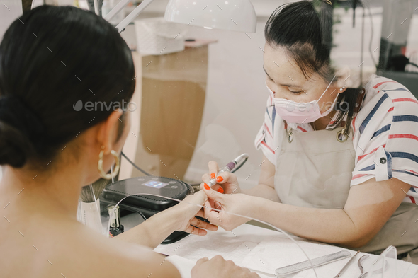 Asian women clients getting a manicure in nail salon, with protective screen, beauty concept