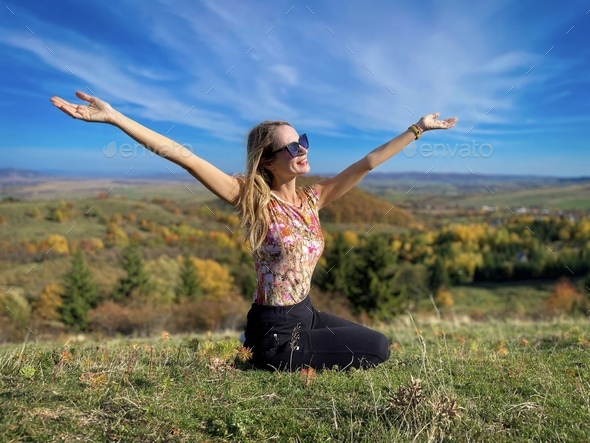 Young woman with her arms outstretched sitting down on the grass ...