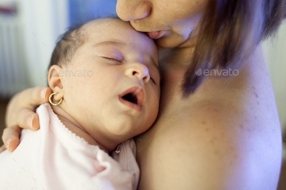 Mother kissing her newborn baby girl. Sleeping baby in the hands of his mother.