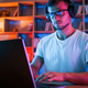 Man in glasses and white shirt is sitting by the laptop in dark room with neon lighting - PhotoDune Item for Sale