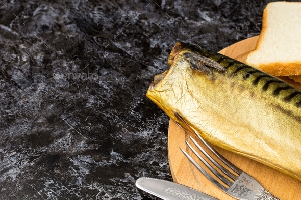 Smoked mackerel without head with fork knife cutting board bread on black background. copyspace top