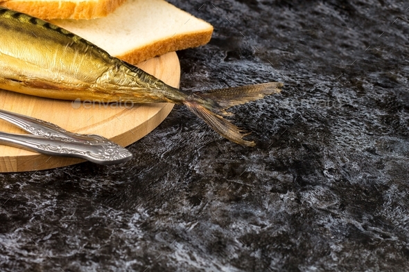Smoked mackerel without head with fork knife cutting board bread on black background. copyspace top