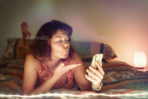 Woman on the bed with mobile phone have video call and send blowing kiss