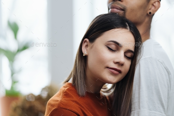 Woman head resting on her man shoulder. She feels safe and seems happy.
