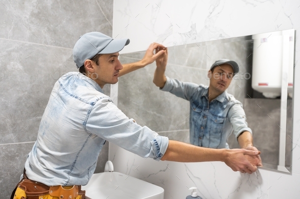 Man installing a mirror on wall in his renewed bathroom