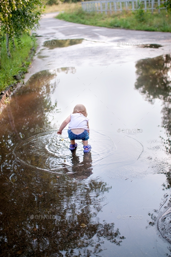 Cute little girl playing in puddle and walking under rain at summer