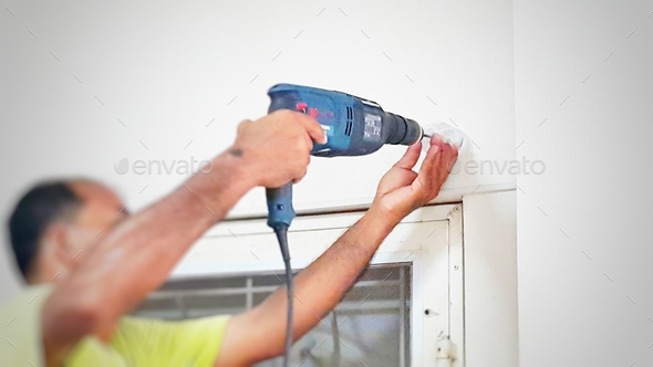Man with yellow shirt drilling house wall to improvement it blur background