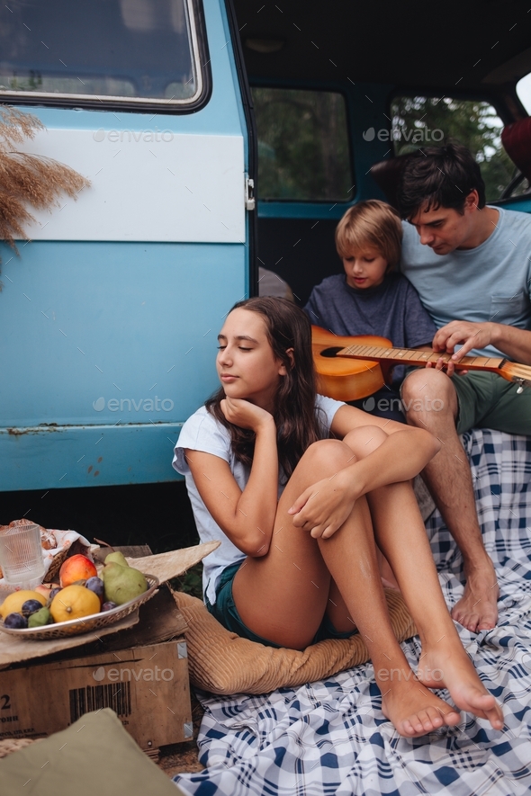 Happy family. Father with son and daughte sitting in camping trailer and boy play the guitar