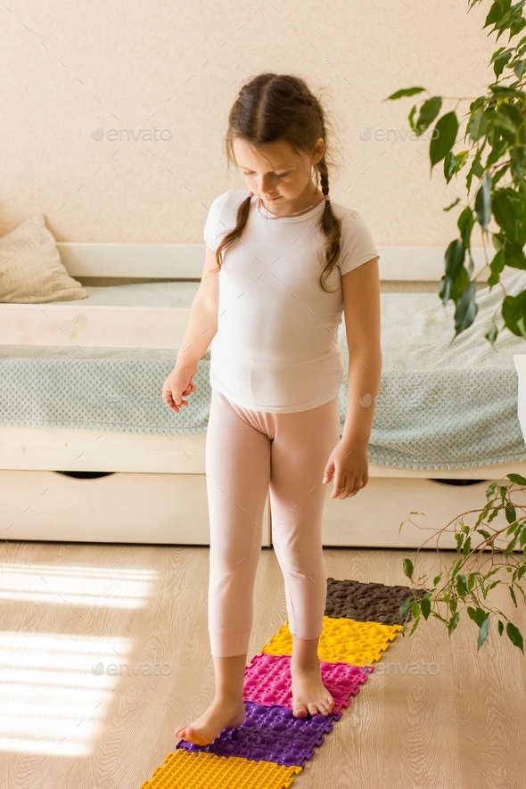 Cute little girl walks on orthopedic massage mat. Foot massage for child. Exercises for legs on carp