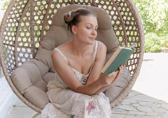 A woman sitting in a chair cocoon and reading a book