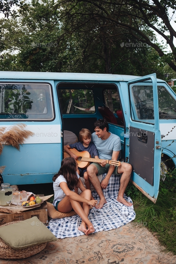 Happy family. Father with son and daughte sitting in camping trailer and boy play the guitar