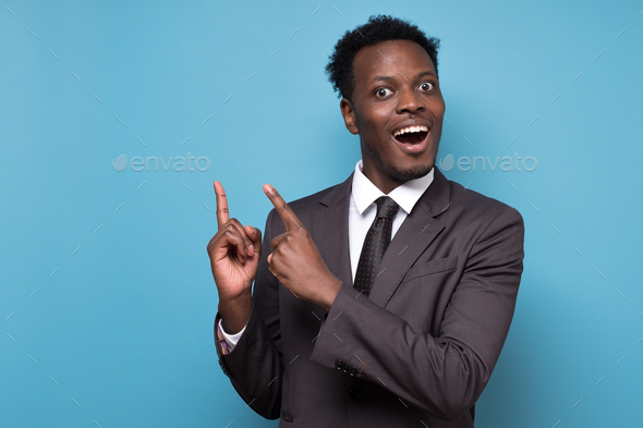 Funny young african american man in suit pointing index fingers aside up.
