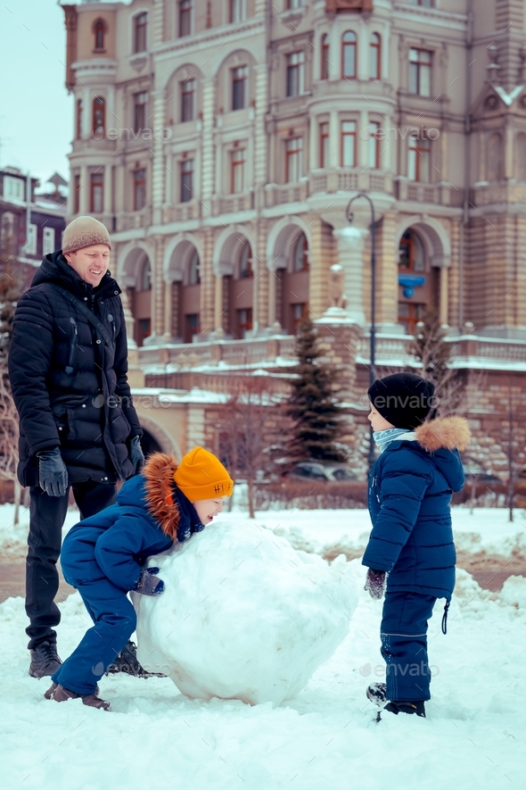 Dad with children makes a big snowman on the street. Games with children in winter.