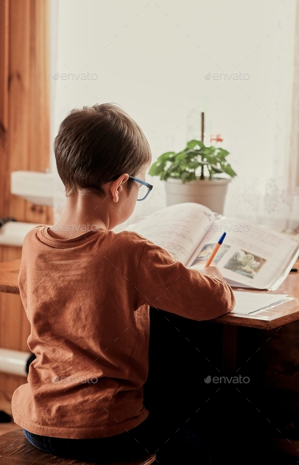 a little boy with glasses does his homework at the table.