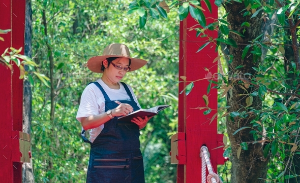Female tourist taking notes of mangrove forest conditions on red wooden bridge in natural park