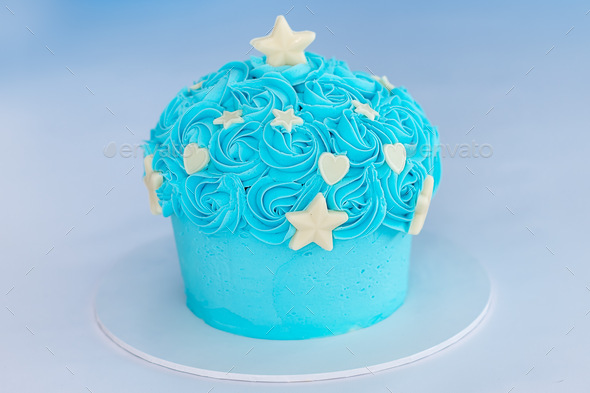A blue giant cupcake with white chocolate stars and hearts on a plain background