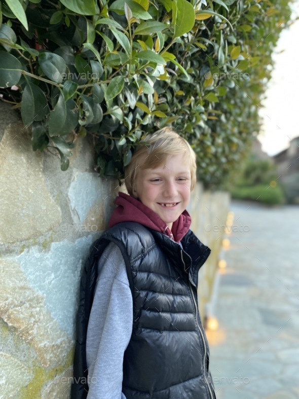 Smiling boy standing near the stone wall Stock Photo by elenabednykh