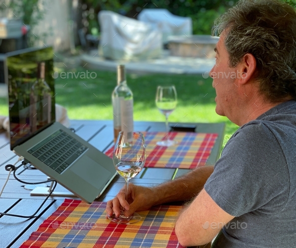 Older white man outside, white wine glass, on a virtual zoom wine event with wine bottle reflection