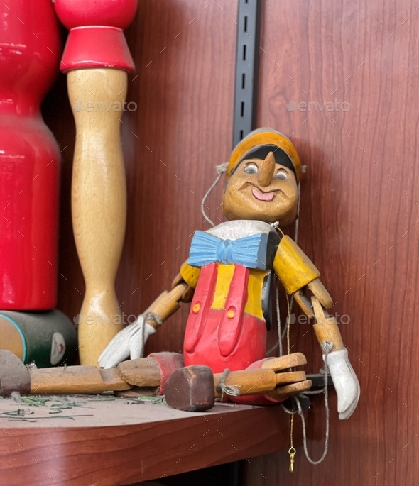 hand carved wooden Pinocchio puppet with string, collapsed on the shelf