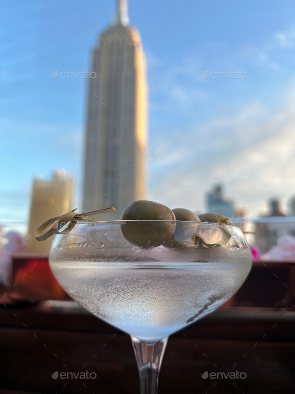 Martini with olives at a rooftop bar and Empire State Building in the background