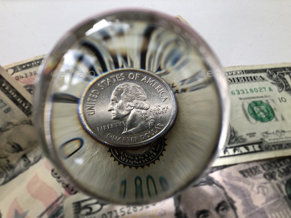 US dollar bills and 25c / quarter dollar coin seen through a crystal ball
