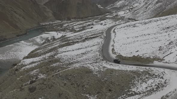 Aerial Drone View Of Black SUV Driving Winding Snow Rocky Mountain Roads In Winter Through Hunza Val alt