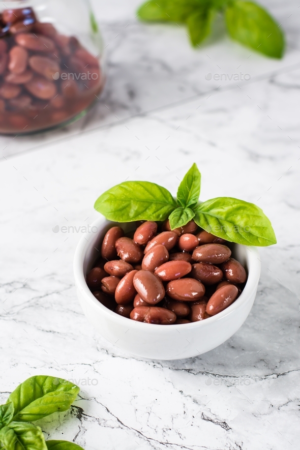 Boiled red beans in a bowl and jar and basil leaves on the table. Meat