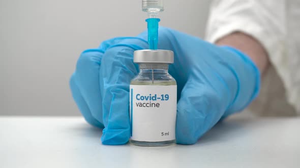 Close up of a doctor in medical blue gloves filling a syringe with a dose of coronavirus vaccine.