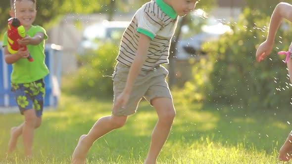 three fun kids boys and girl playing with water guns on green lawn in the backyard at hot summer day