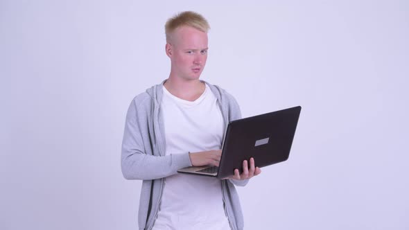 Happy Young Blonde Handsome Man Thinking While Using Laptop alt