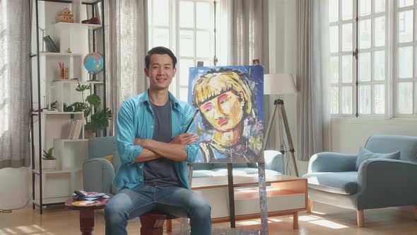 Asian Artist Man Crossing His Arms, And Smiling After Finish Painting On The Canvas alt