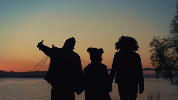 Parents Silhouette Holding Hands Going to River Shore with Daughter Sunset View alt
