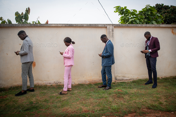 a group of well-dressed young Africans use their smartphones in line while keeping a safe