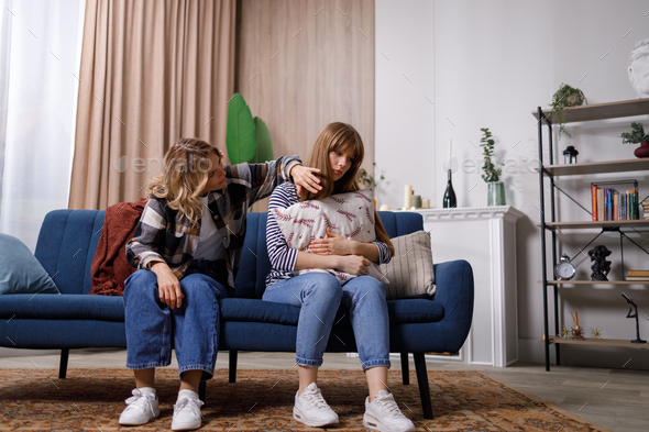 Worried mother tries to calm her offended daughter who sitting on the couch in living room