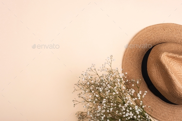 Female summer straw hat and gypsophila plant on neutral beige background.  Top view, flat lay