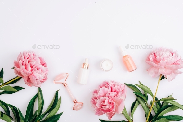 Dropper bottles with cosmetic oil and serum, facial roller, cream jar and peony flowers on white