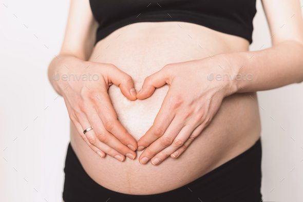 Woman hands making heart on pregnant belly. Pregnancy, maternity