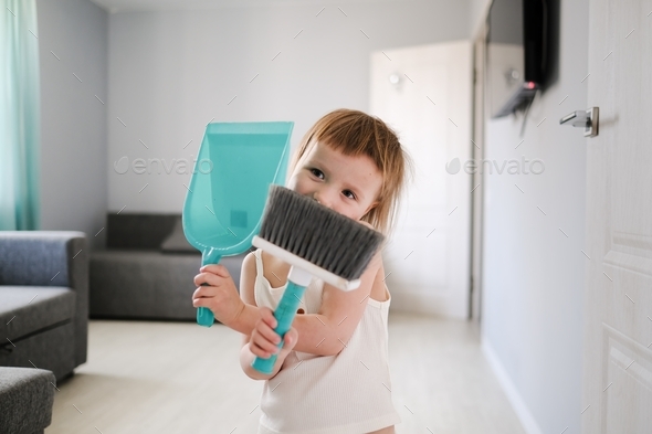 Cute European child with blue scoop for garbage and brush for sweeping floor