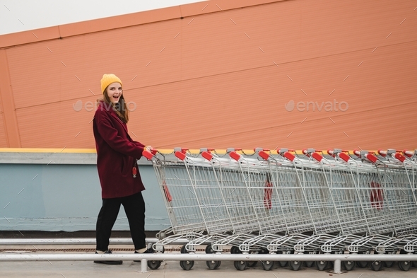 Young beautiful woman in a burgundy coat and yellow hat walks on the roof of supermarket parking lot