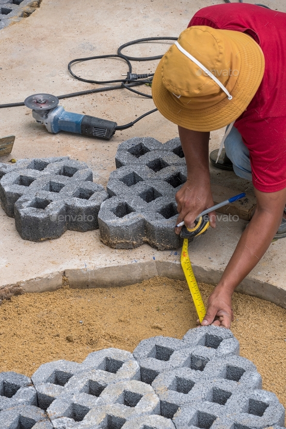 Construction worker measuring gaps in walkway for cut turf stone block