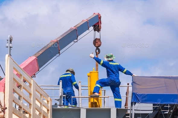 2 engineers with crane truck transferring yellow hydraulic cylinder into sand suction dredger ship