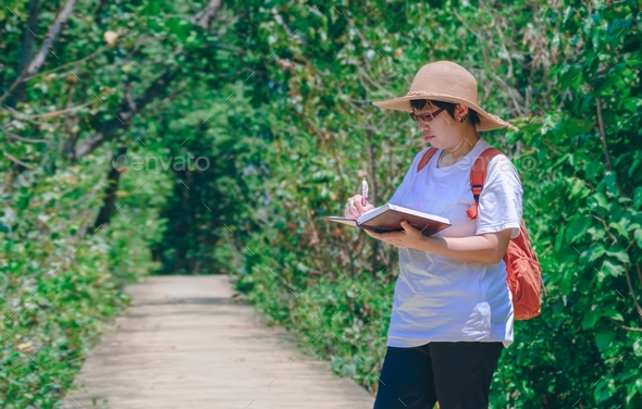 Female tourist taking notes on walkway while ecotourism in mangrove forest at natural parkland