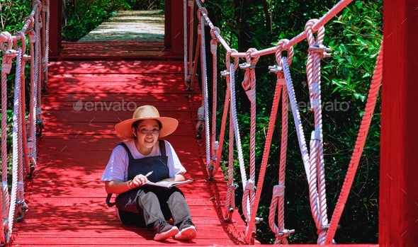 Smiling female tourist looking at camera while sitting on suspension bridge at natural parkland