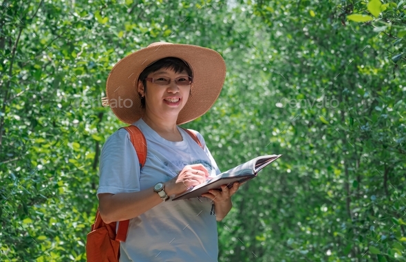 Portrait of female tourist smiling and looking at camera while taking notes in natural parkland