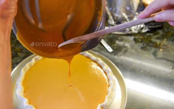 Freshly prepared pumpkin pie custard is poured into a pie crust, ready to be baked off.