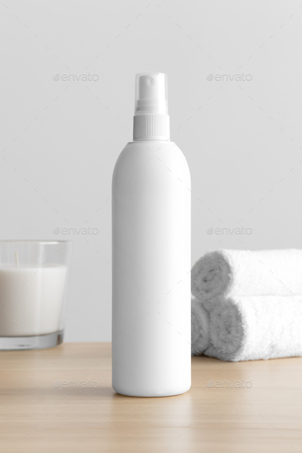 White cosmetic spray bottle mockup with a candle and towels on the wooden table.