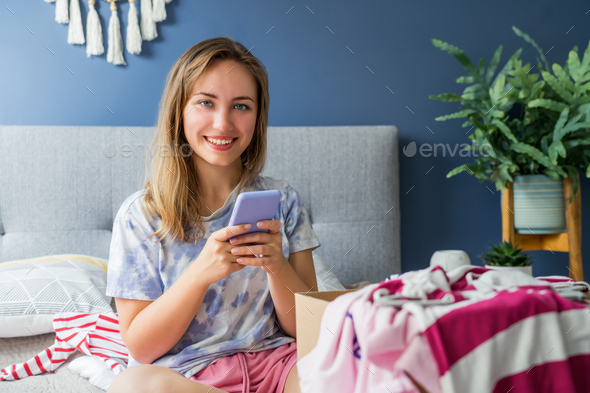 Smiling woman using smartphone to find places where to donate or sale clothes. Decluttering